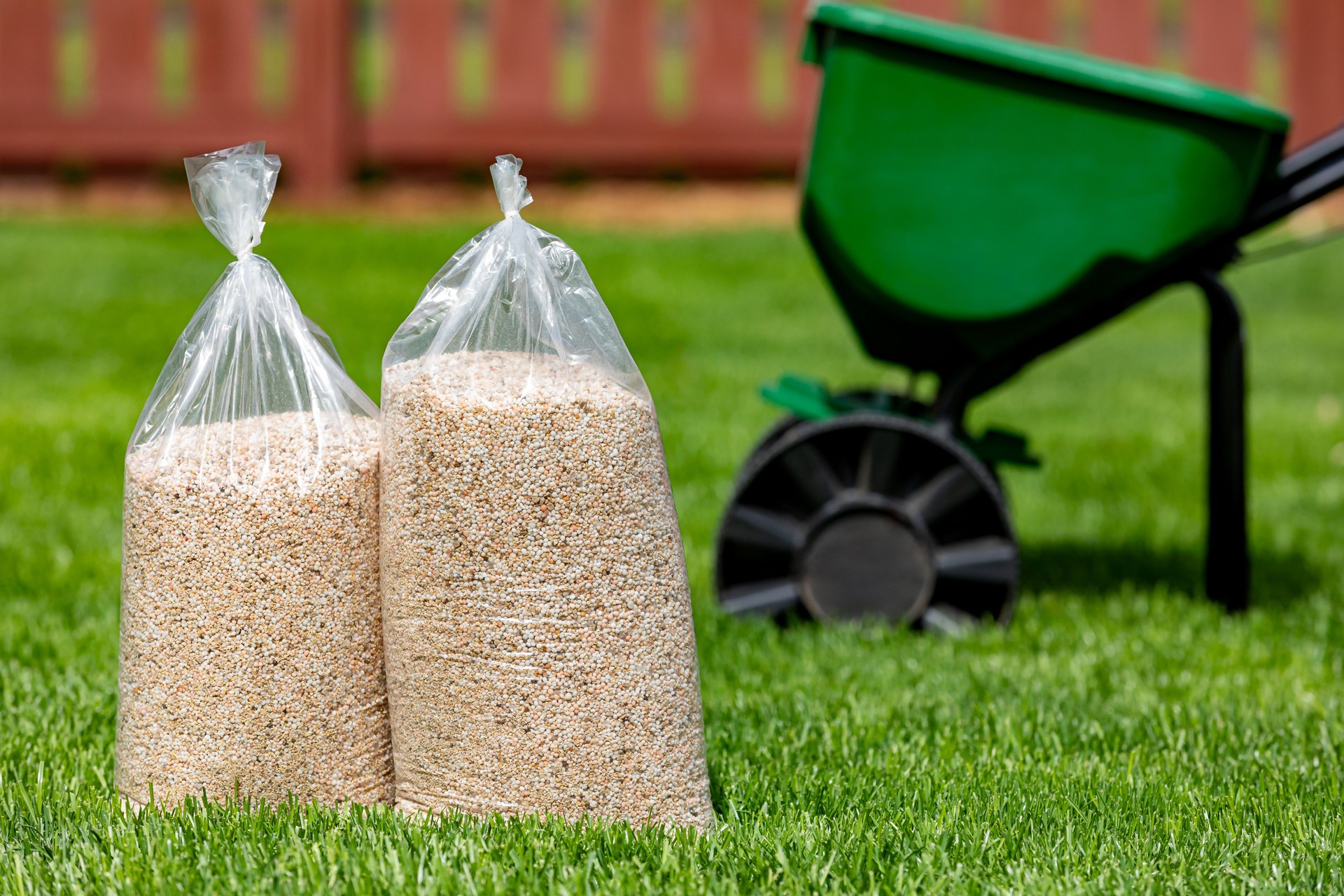 Bags of lawn fertilizer and herbicide with broadcast spreader in yard with healthy grass. Lawn care, weed control and landscaping concept.